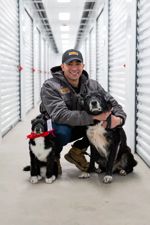 Eli from Responders Storage kneeling with two black and white dogs in the indoor storage hallway